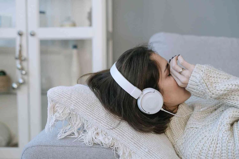 Frau liegt mit kopfh&ouml;rern auf der coach und wischt durch ihr gesicht