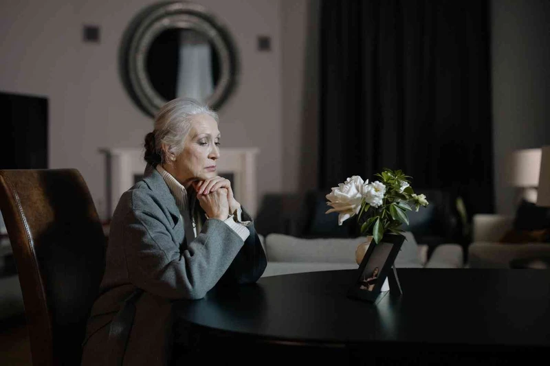 &Auml;ltere Frau sitzt traurig am Tisch und guckt auf ein Bild